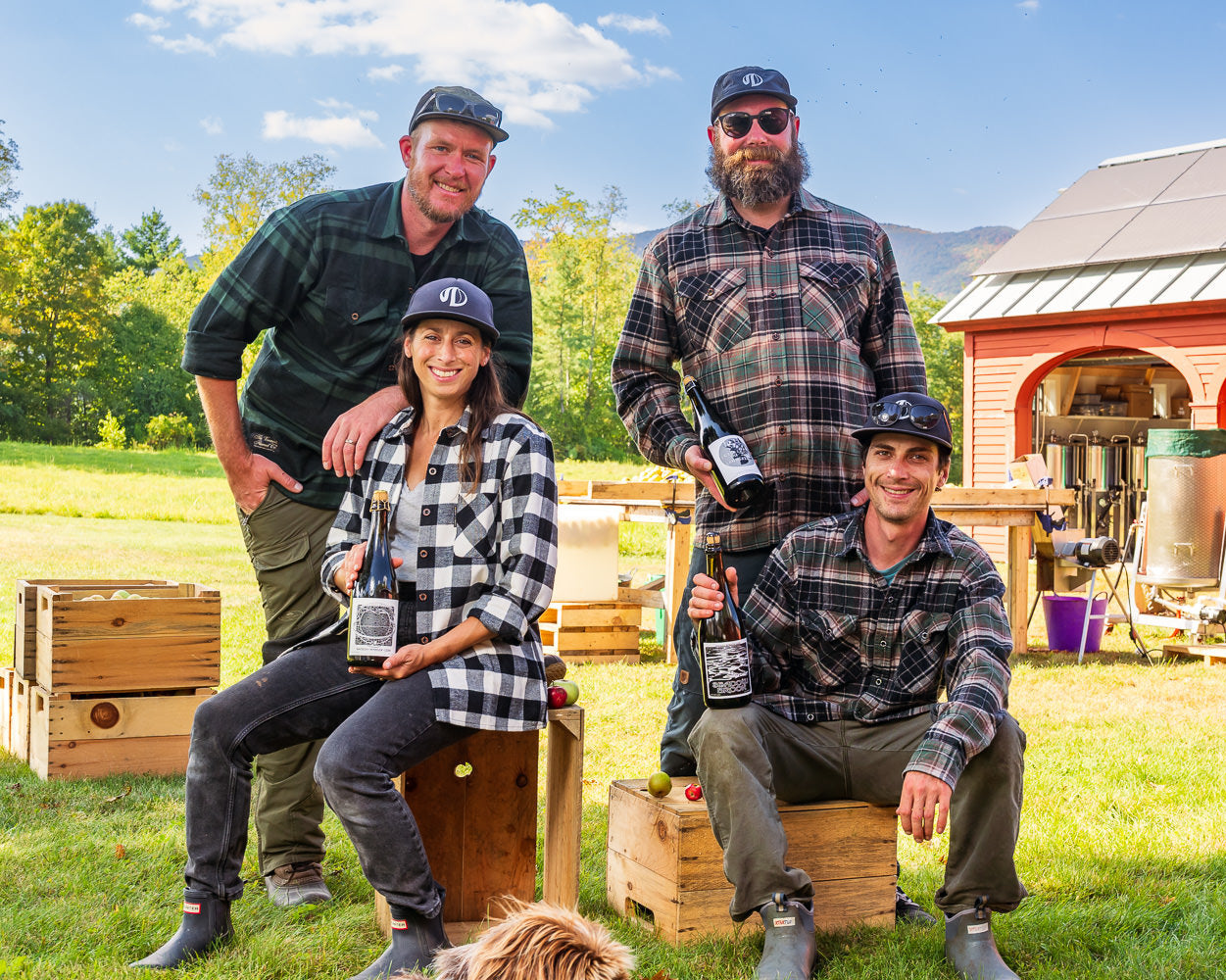 Four people posing outdoors with a barn and greenery in the background