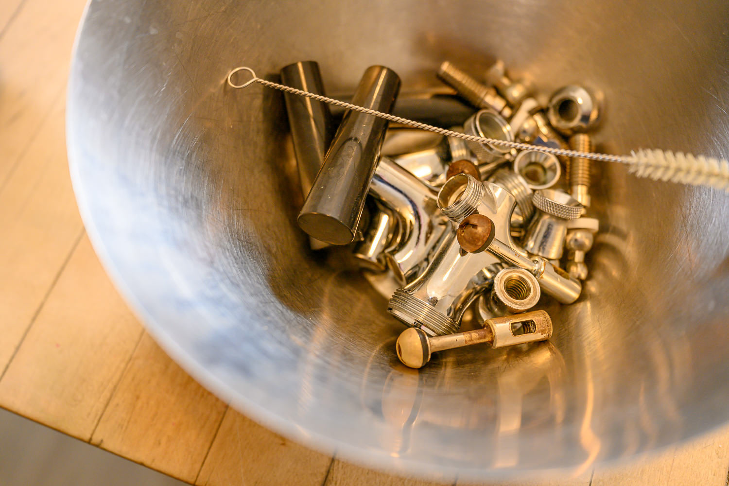 Metal bolts and nuts in a metal bowl on a wooden surface